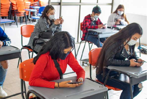 Estudiantes de RedInncol en un aula con sillas muy separadas entre una y otra y estudiando por medio de su celular